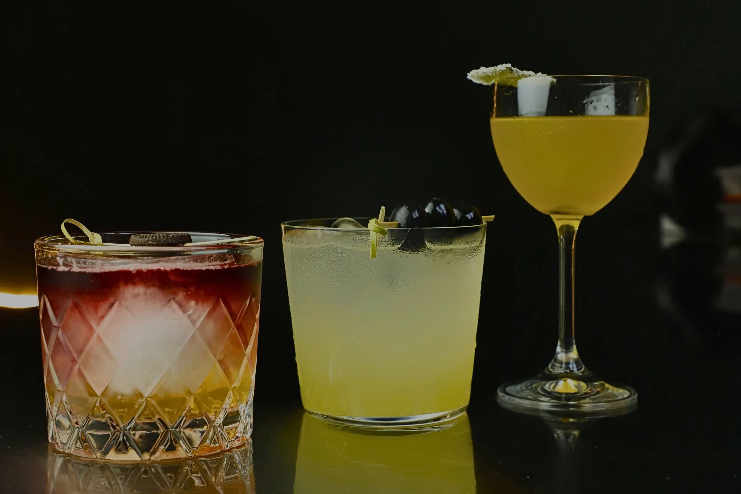 Tres cócteles de autor de STILLROOM sobre fondo oscuro: vaso tallado, hielo y garnish de la casa