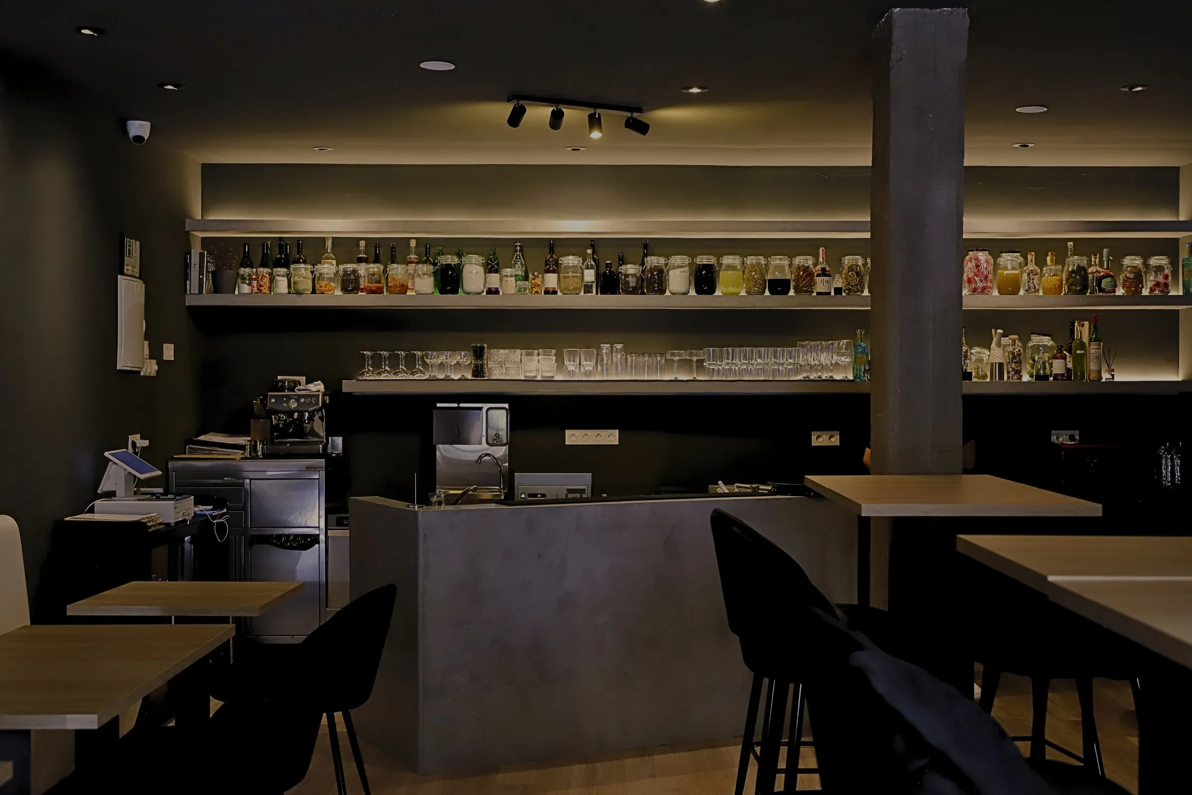 La sala de STILLROOM de noche: barra de microcemento y estantes retroiluminados con los fermentos de la casa, en Los Jerónimos (Madrid)
