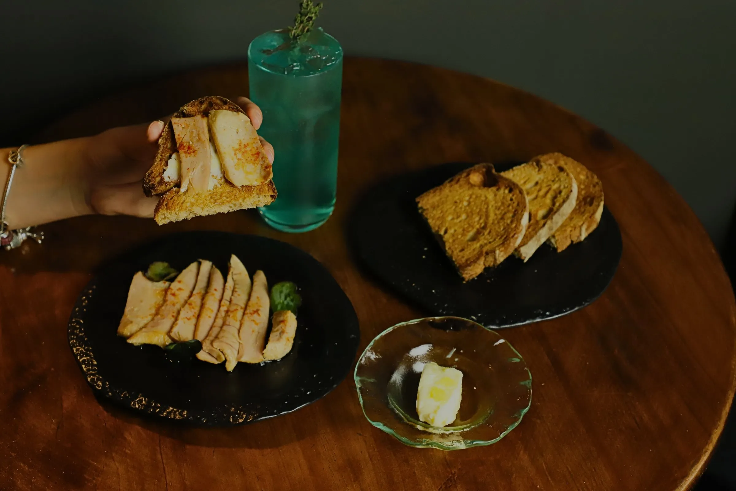 Ventresca de atún con mantequilla y pan tostado, junto a un cóctel azul de la casa, sobre una mesa de STILLROOM