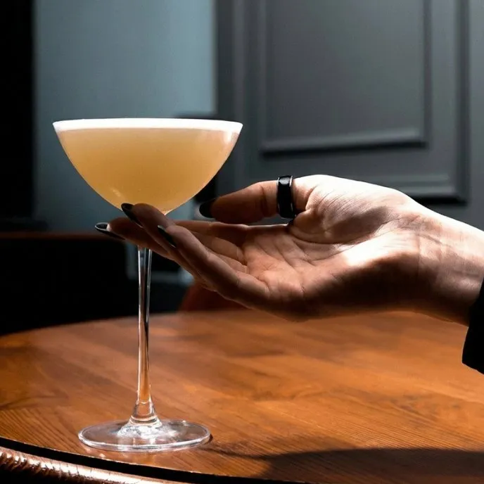 A hand holds a coupe glass with a clarified cocktail on the Stillroom table