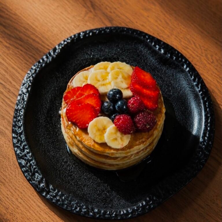 Tortitas con plátano, fresas, arándanos y frambuesas servidas en plato negro en el brunch de Stillroom, Madrid